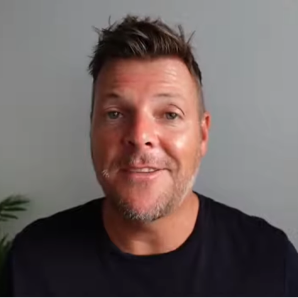 Smiling man with short hair and a trimmed beard wearing a black shirt against a gray background.