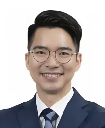 Portrait of a smiling young Asian man wearing glasses and a dark suit with a white shirt and striped tie.