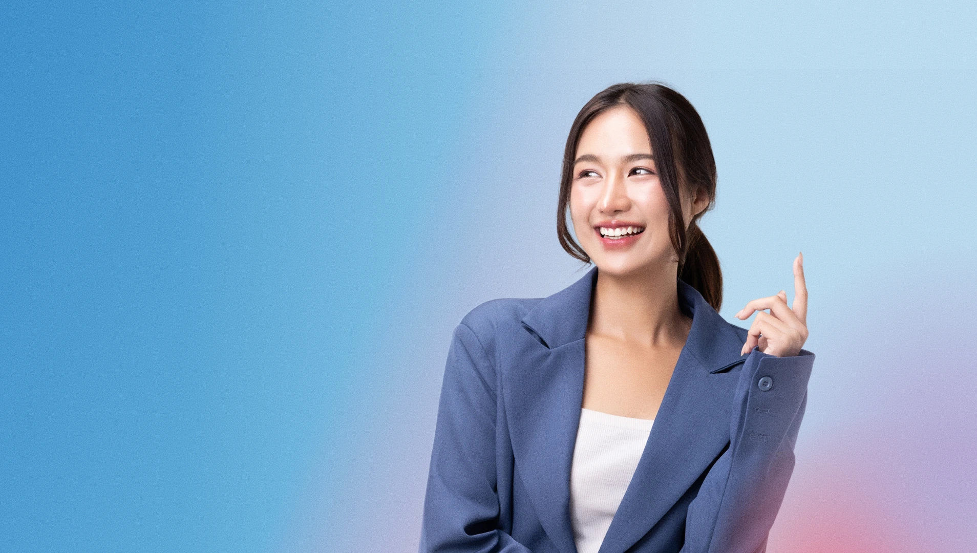 Smiling young woman in a blue blazer pointing upwards against a blue gradient background.