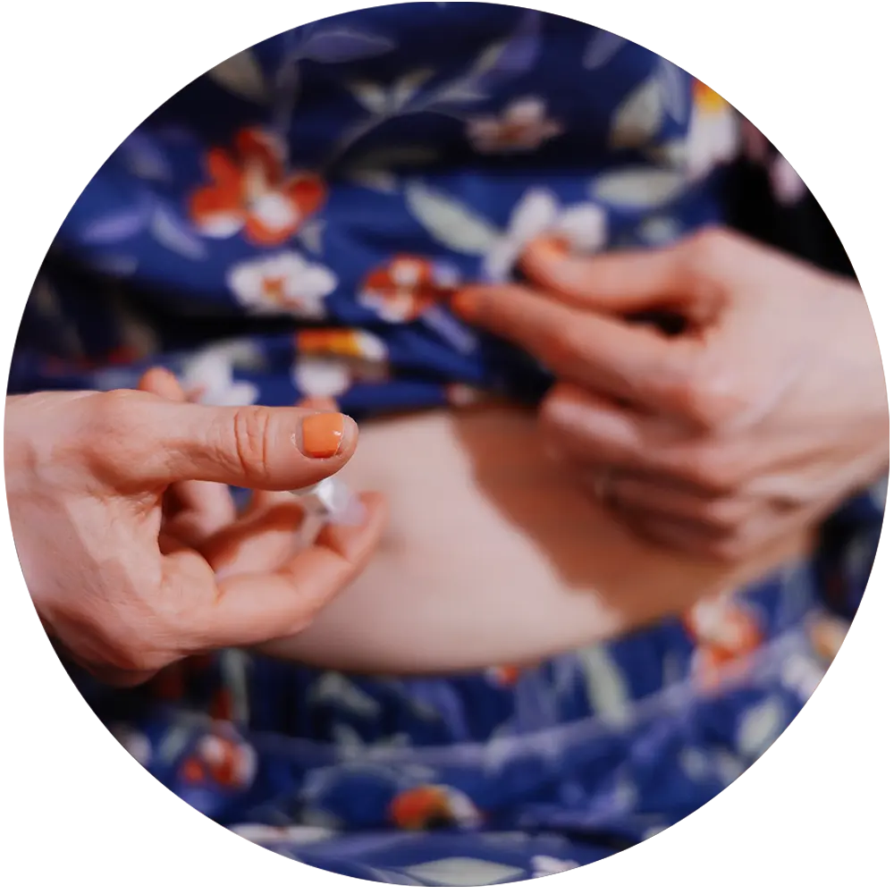 Person preparing to inject medication in the abdomen, lifting floral-patterned clothing.