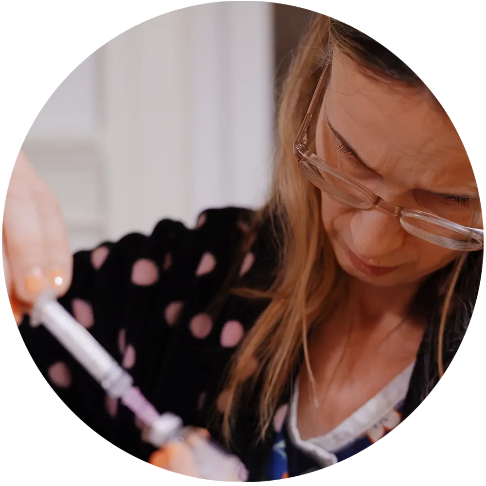 Woman wearing glasses carefully preparing a syringe with medication or vaccine.