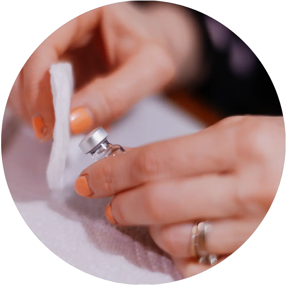 Close-up of hands holding a small medicine vial and a cotton pad on a white surface.