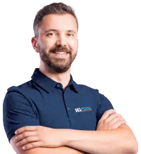 Smiling man with short brown hair and beard wearing a navy blue polo shirt with crossed arms.