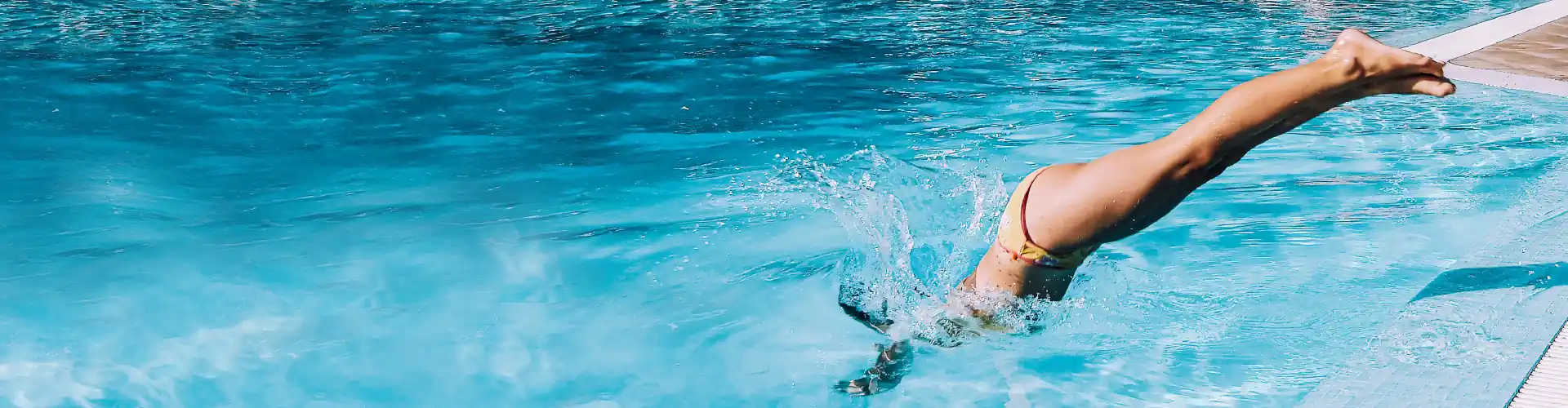 Person diving headfirst into a bright blue swimming pool from the edge.
