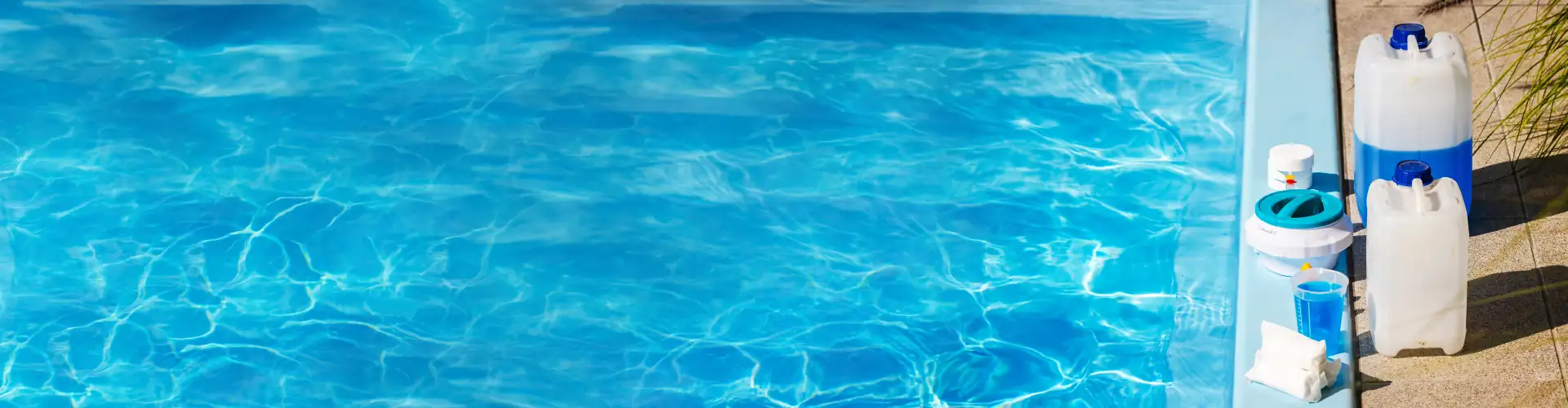 Bright blue swimming pool water with pool maintenance chemicals and test kits on the pool edge.