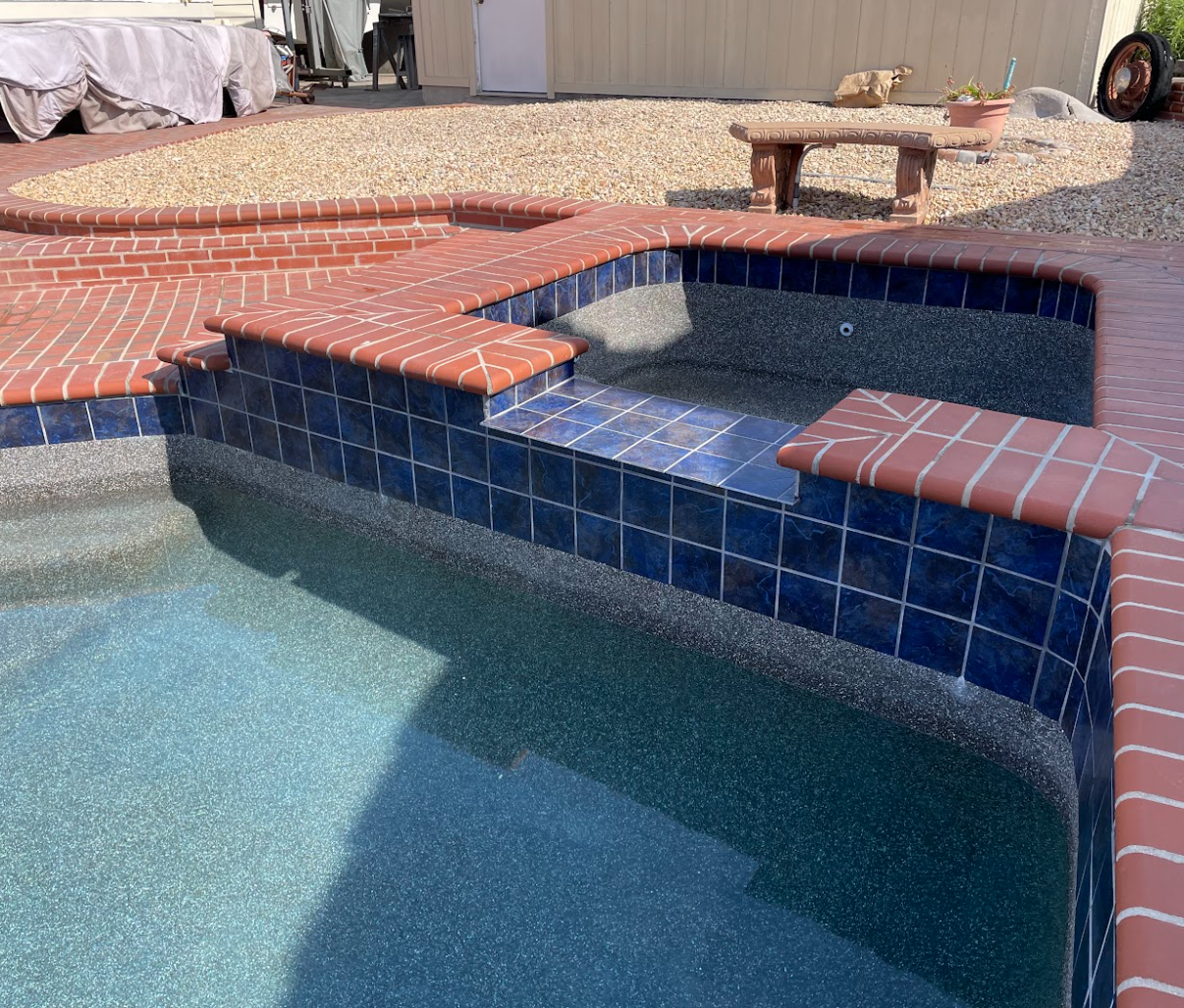 Blue tiled swimming pool with brick accents in backyard setting