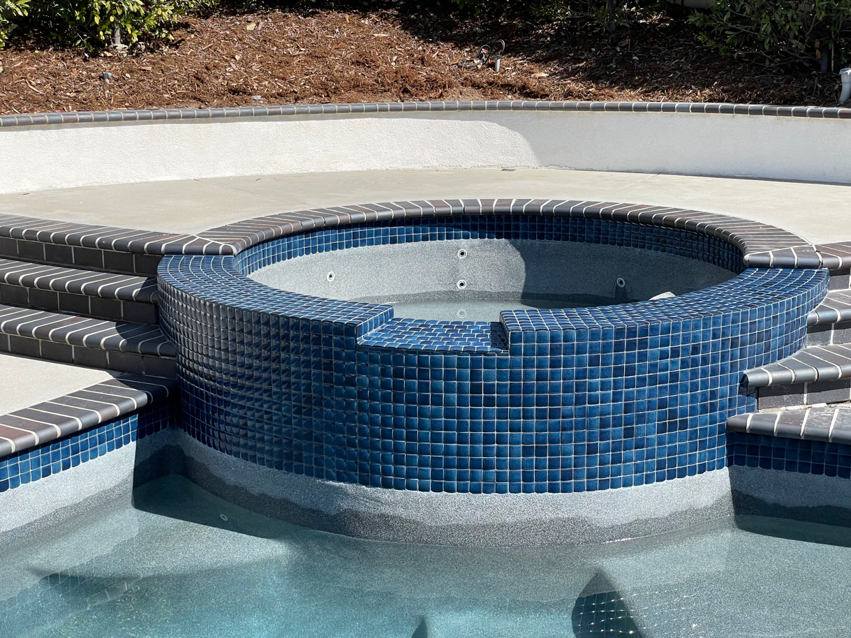 Circular blue-tiled hot tub with attached concrete pool deck