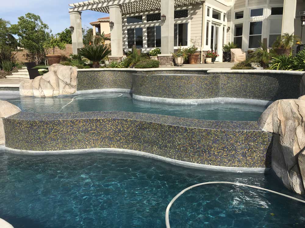 Luxurious multi-level pool with mosaic tiles and rock features near modern home