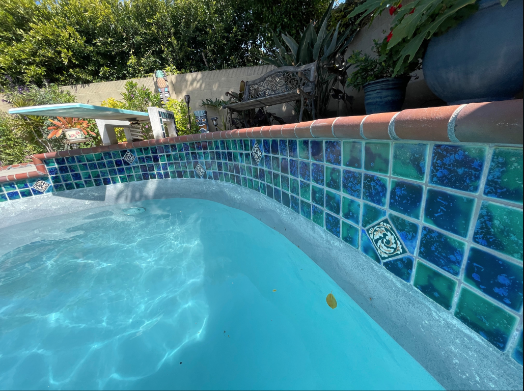 Swimming pool with blue-green mosaic tiles and lush garden background