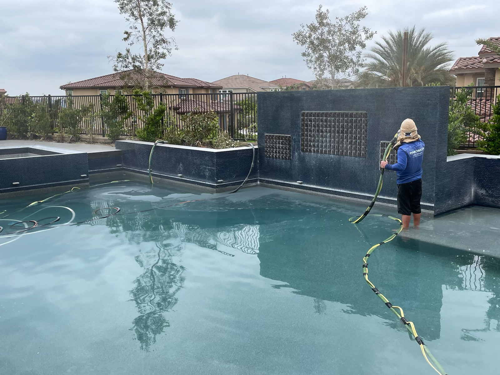 Pool technician cleaning a blue tiled swimming pool with a long hose