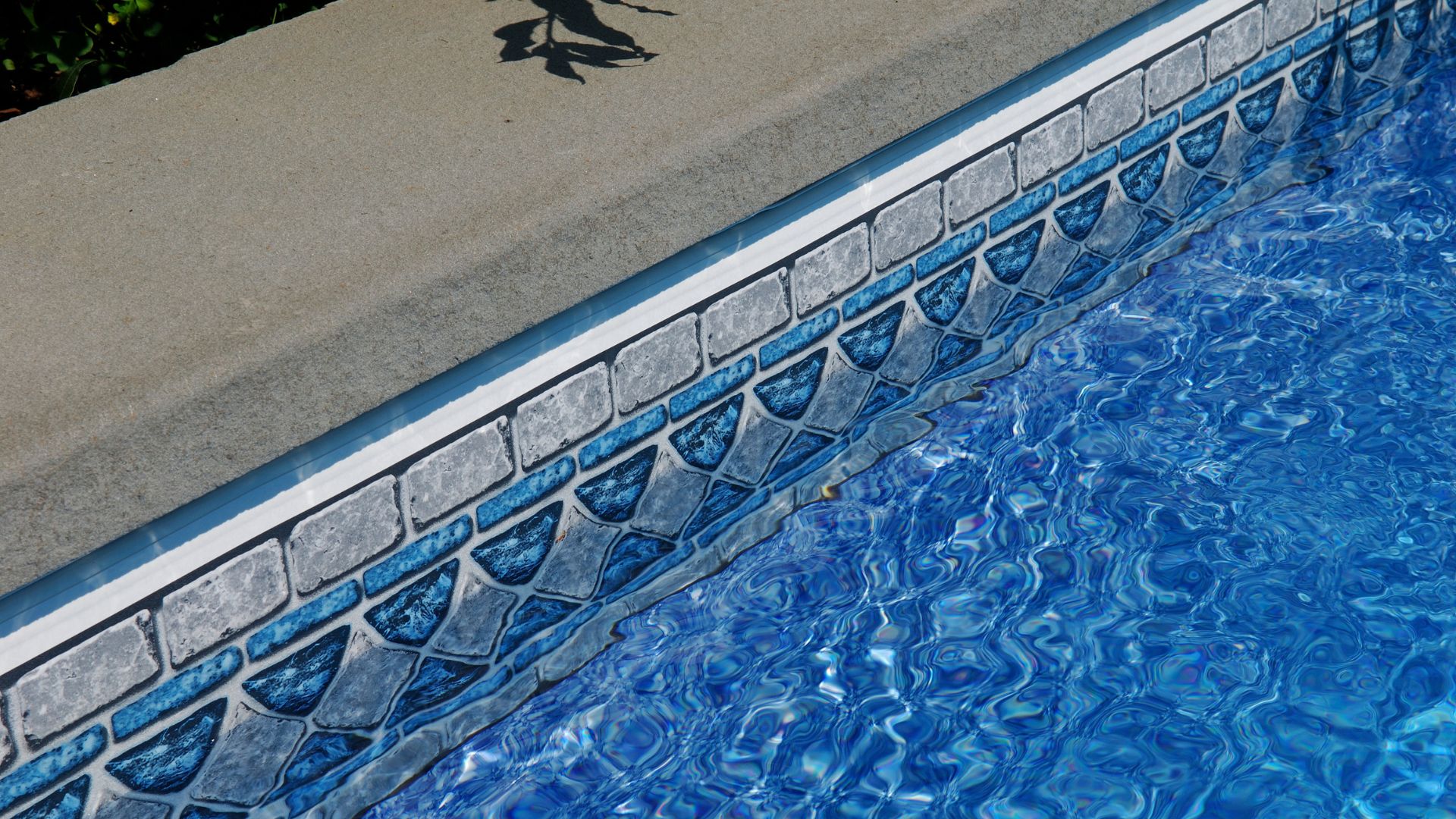 Blue swimming pool with stone tile border and rippling water surface