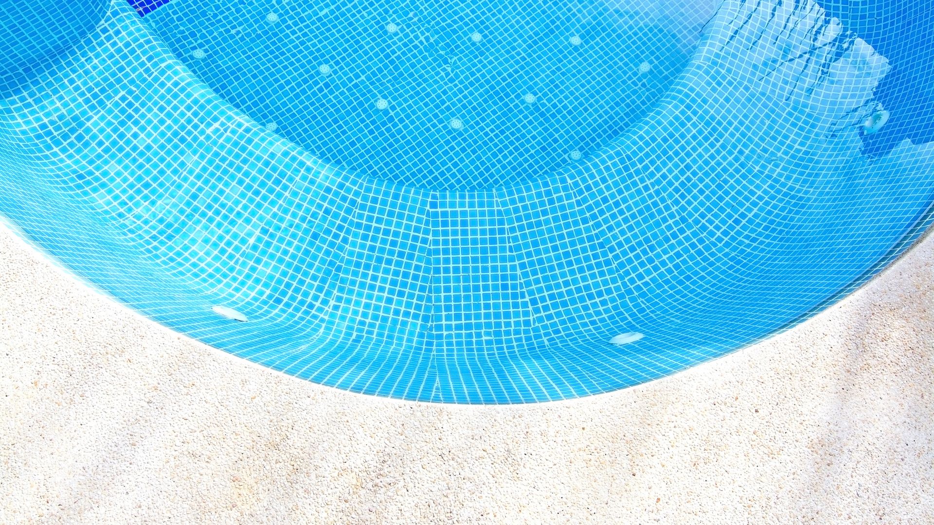 Curved blue mosaic swimming pool with white tiled edge and sandy border