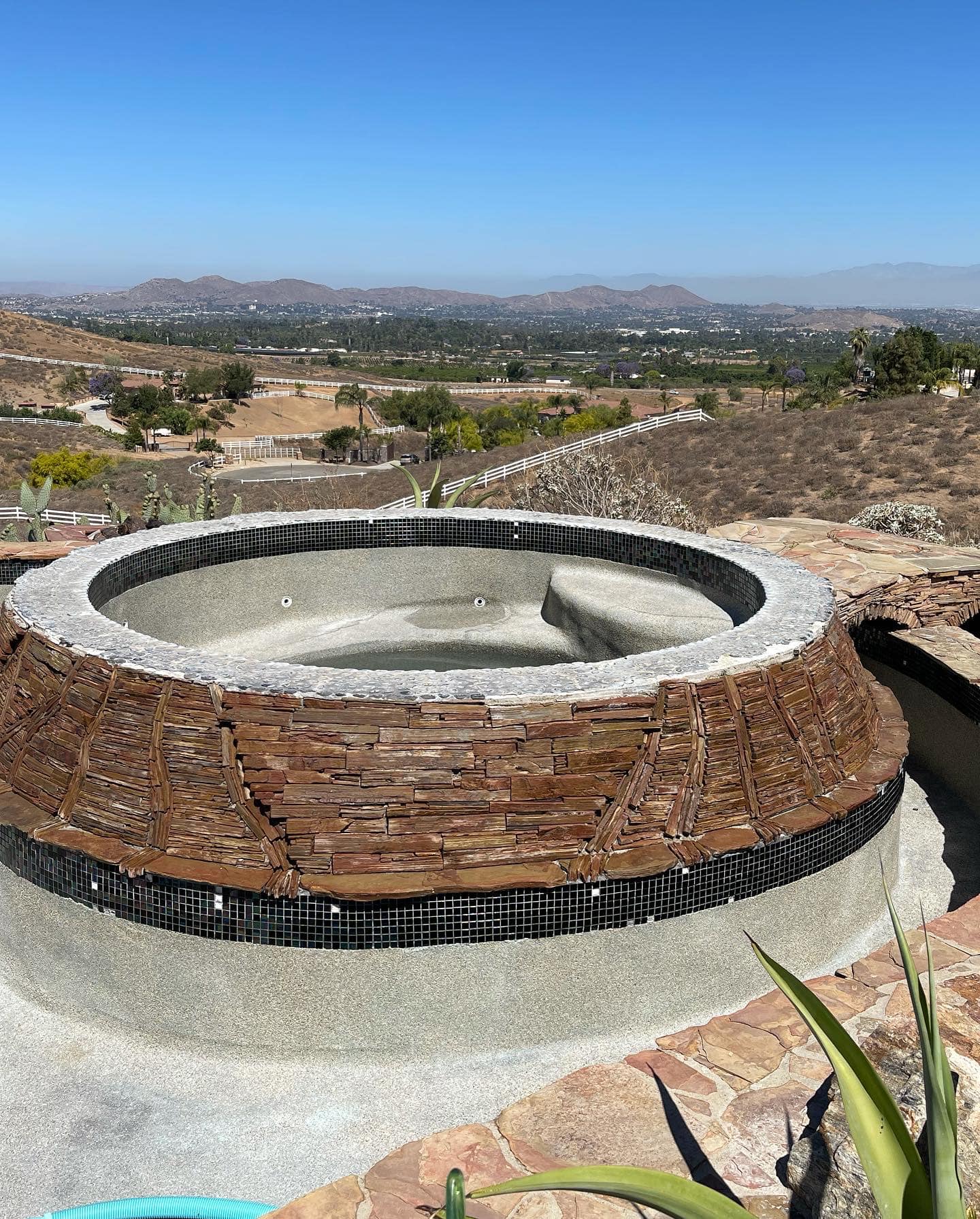 Circular stone jacuzzi with rustic wood exterior overlooking mountainous landscape