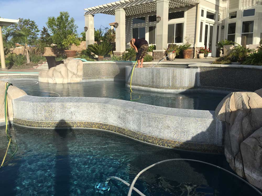 Luxurious backyard pool with rock features and mosaic tiles being cleaned