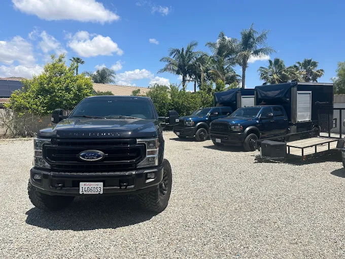 Black Ford trucks parked on gravel with palm trees in background