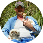 Smiling woman with glasses, dark hair, and a tattoo on her arm resting her chin on her hand.