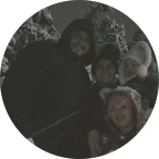 Smiling person with glasses wearing a black suit jacket and white shirt seated in front of a decorative metal headboard.