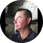 Smiling woman with long dark hair wearing a blue top and a silver necklace in a living room.