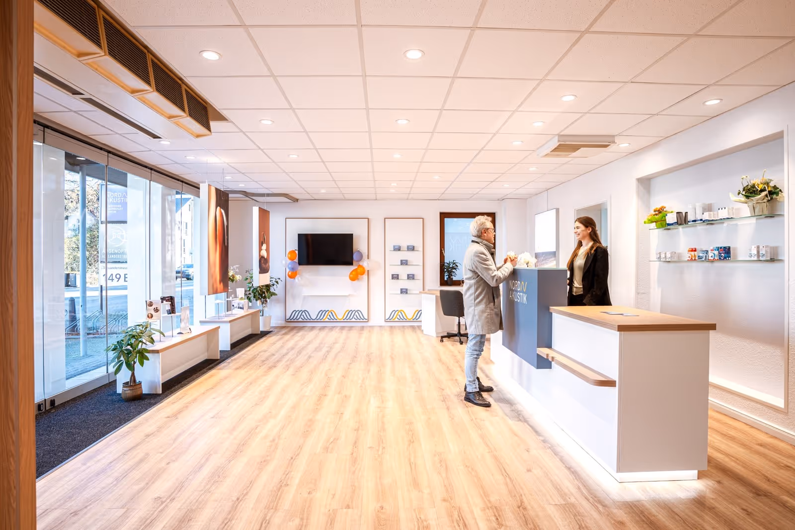 Junger Mann in blauem Pullover und beiger Hose, der auf einem gepflasterten Platz vor einem gelben historischen Gebäude spaziert.