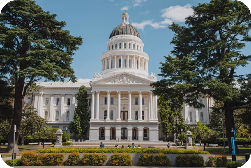 Front view of a large white domed capitol building surrounded by trees and a lawn.