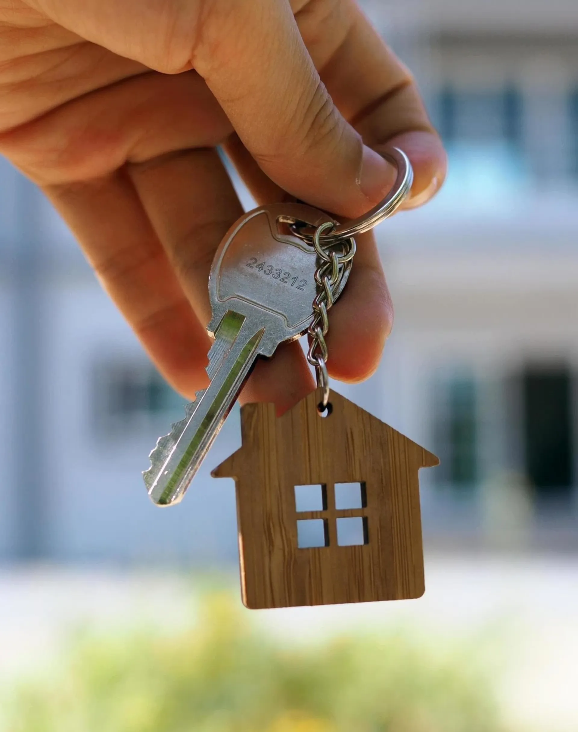 Hand holding a house-shaped wooden keychain and a silver house key.