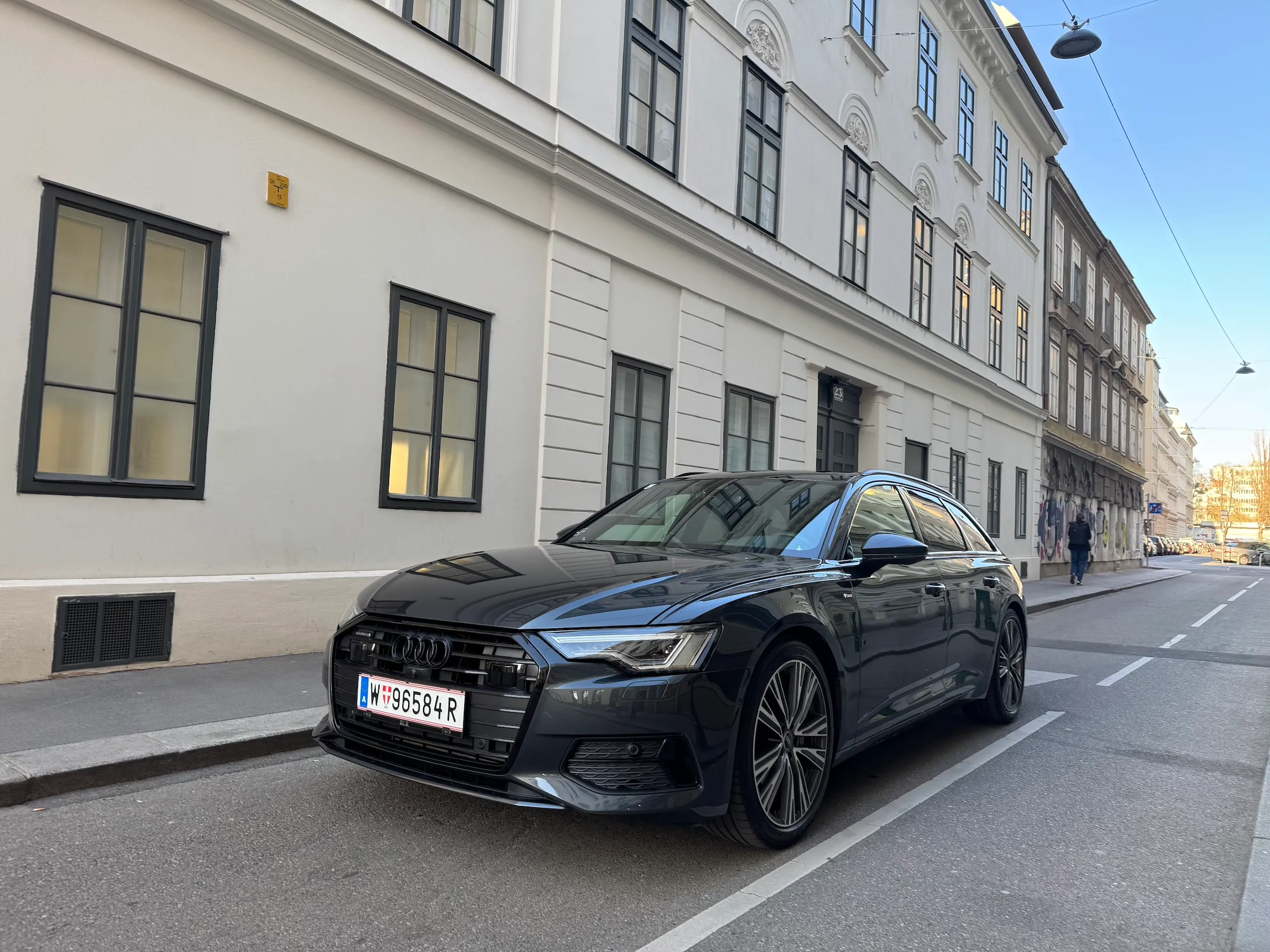 Black Audi sedan parked on a city street beside a white building with multiple windows.