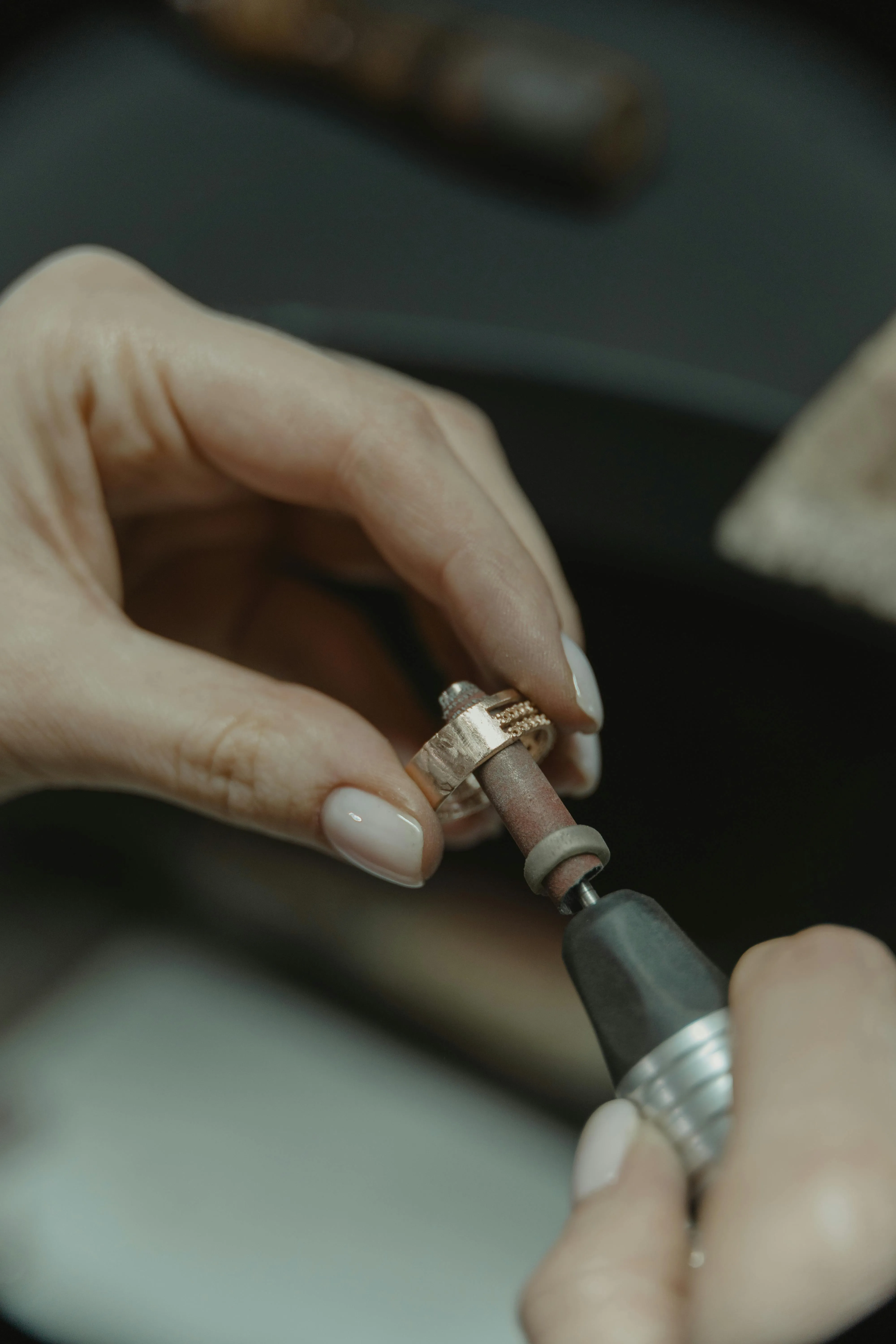 Close-up of hands polishing a gold ring using a rotary tool with a sanding attachment.