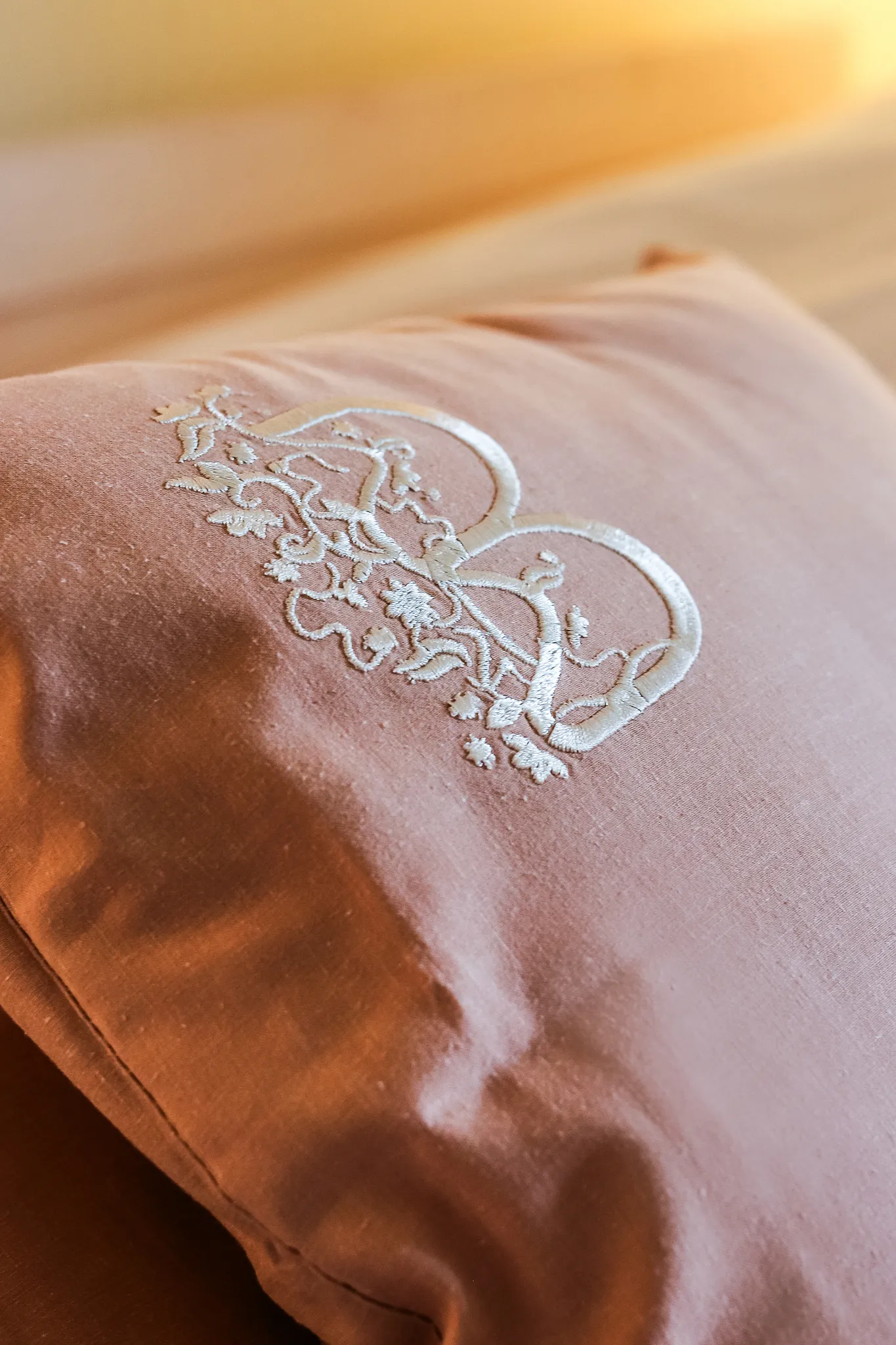 Różowa poduszka z białą haftowaną ozdobą w kształcie serc i kwiatów na jasnym tle. Bednarzówka