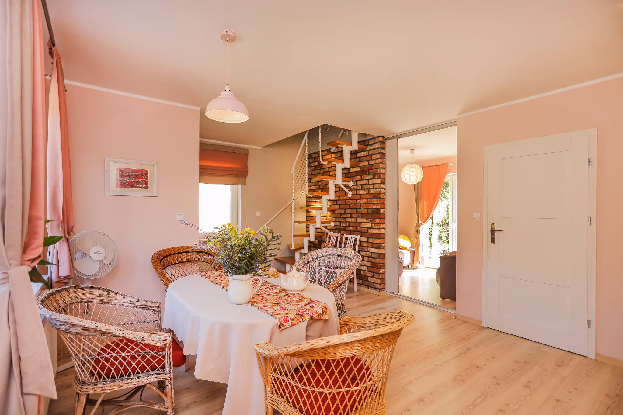 Przytulny salon z różową sofą i fotelem, oknem balkonowym z zasłonami i telewizorem na ścianie.