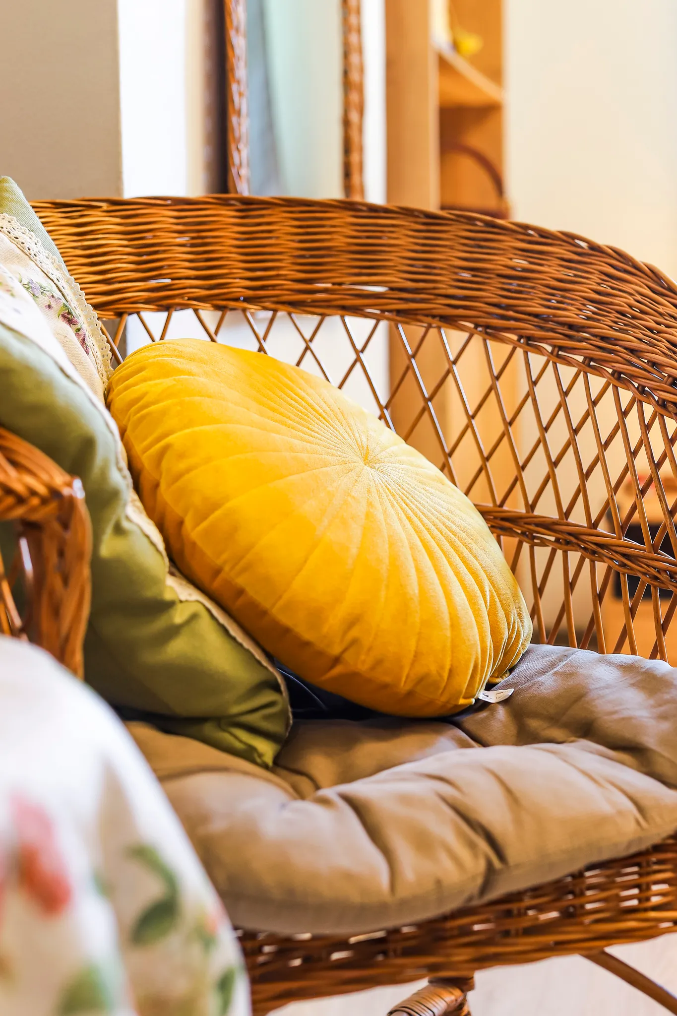 Przytulna sypialnia z łóżkiem, żółtymi zasłonami, telewizorem na komodzie oraz wiklinowymi meblami przy ścianie z czerwonej cegły.