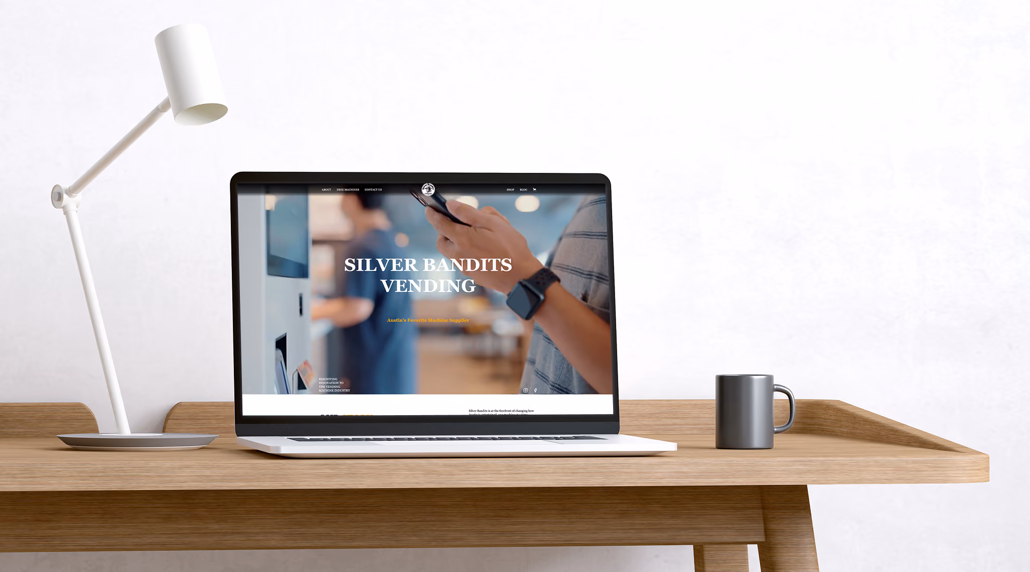 Laptop on wooden desk displaying Silver Bandits Vending website, next to a white desk lamp and gray coffee mug.