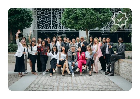 Group of diverse professionals smiling and posing outdoors in front of decorative metal panels and greenery.