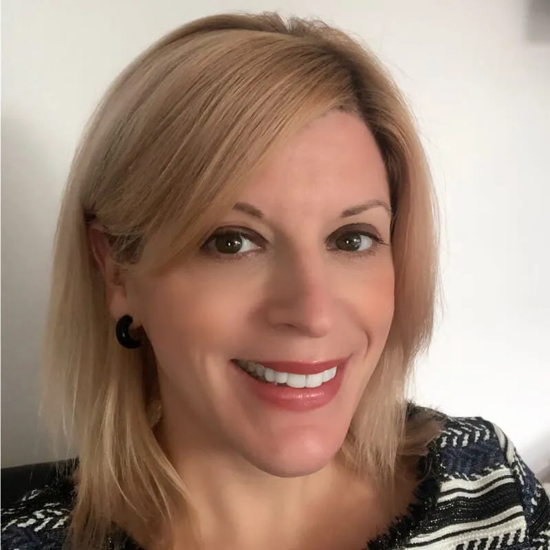 Smiling woman with straight blonde hair wearing black earrings and a striped top.