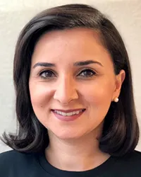 Portrait of a smiling woman with short dark hair and pearl earrings against a neutral background.