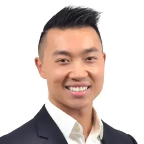 Smiling man with short black hair wearing a dark blazer and white shirt against a white background.