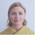 Portrait of a woman with blonde hair wearing a yellow garment against a light gray background.