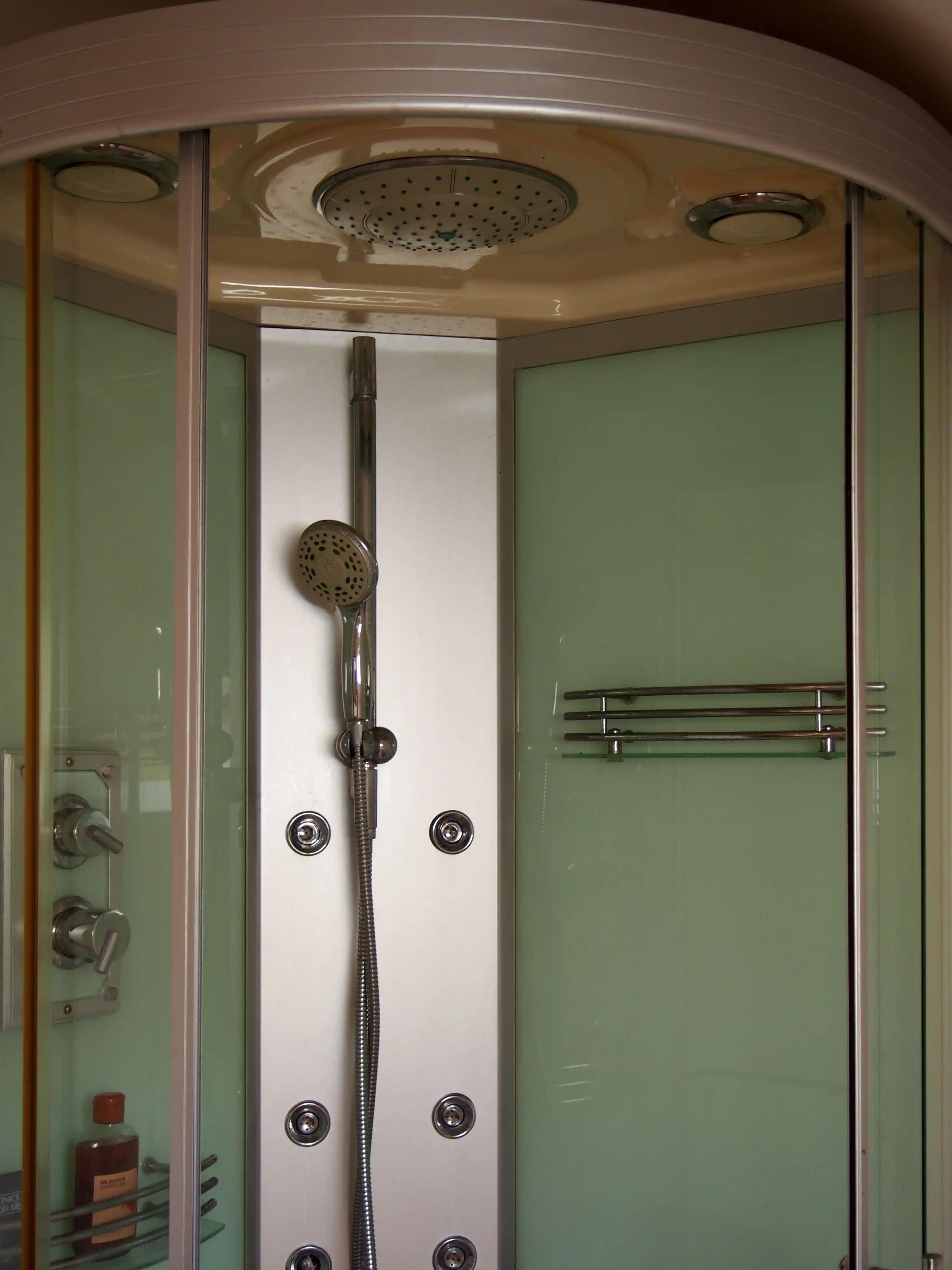 Modern enclosed shower cabin with mounted handheld showerhead, overhead rain shower, and glass shelves.
