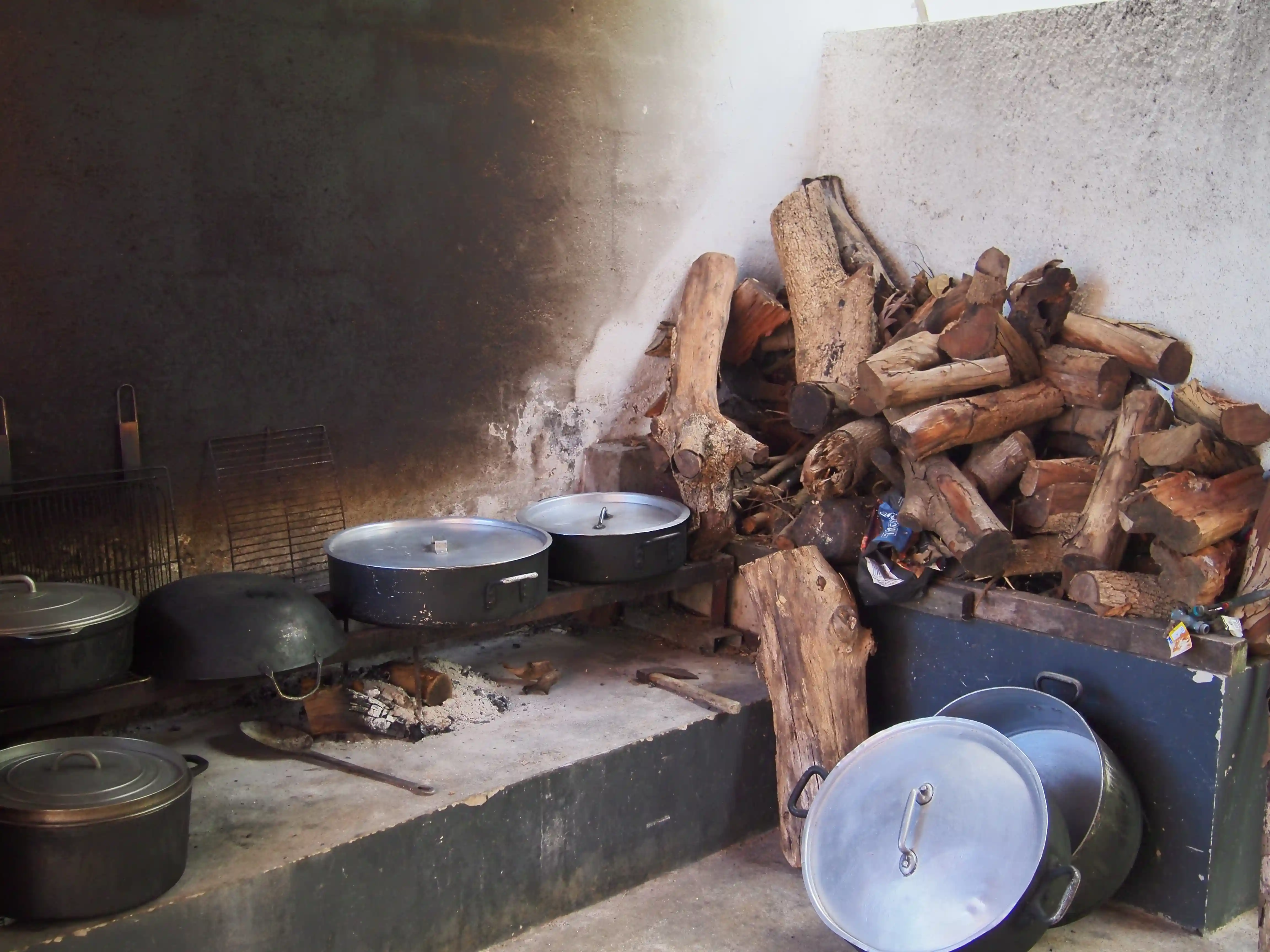 Traditional indoor cooking area with firewood stacked in the corner and large covered pots set over a wood-burning stove.