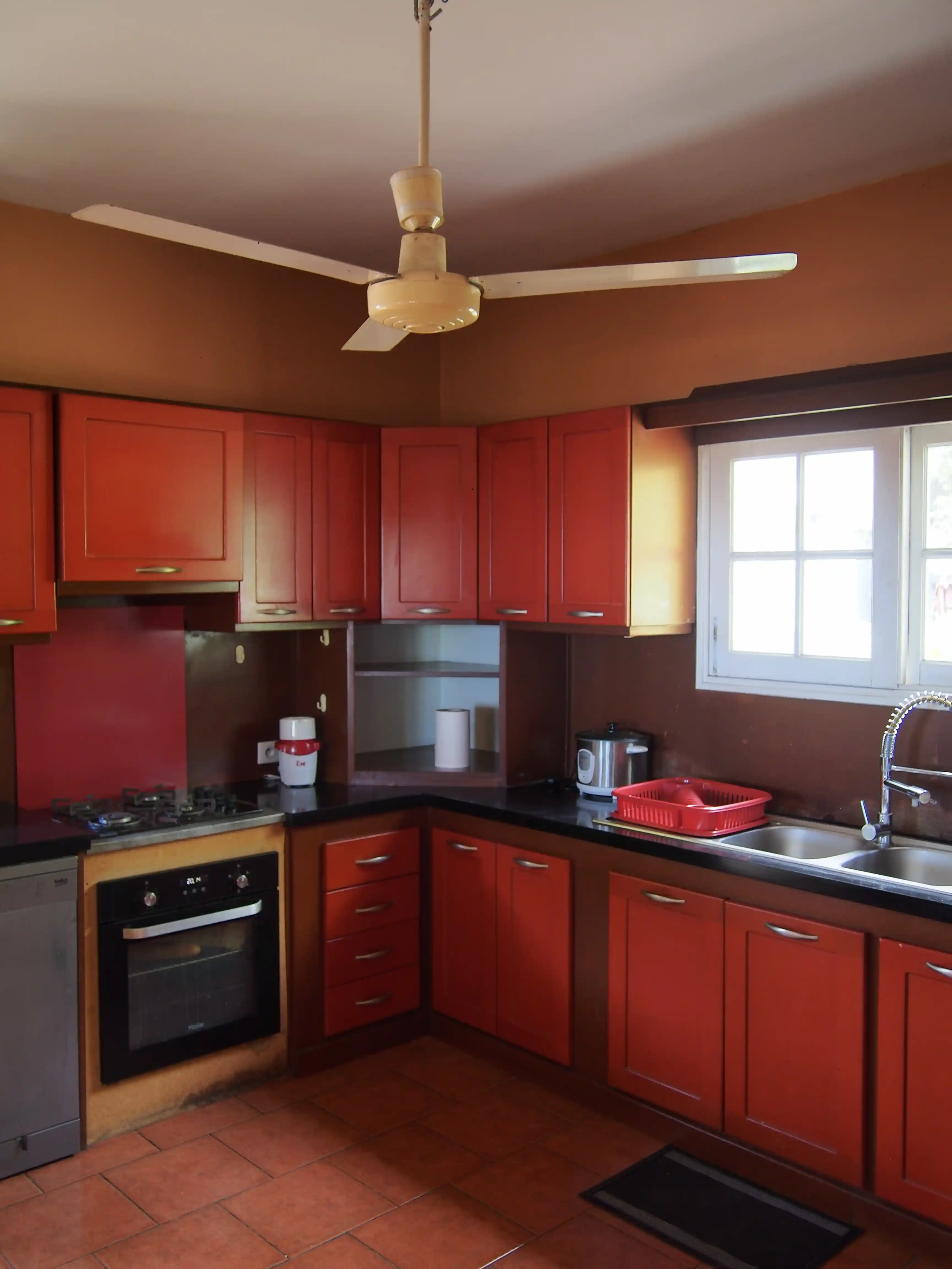 Kitchen with orange cabinets, black countertop, gas stove, oven, double sink, and ceiling fan.
