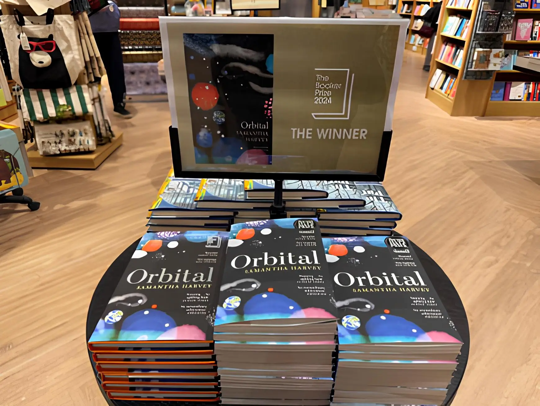 Display of Samantha Harvey's Booker Prize-winning novel Orbital, featuring stacks of the book arranged on a table in a bookstore, accompanied by a promotional sign highlighting its award recognition