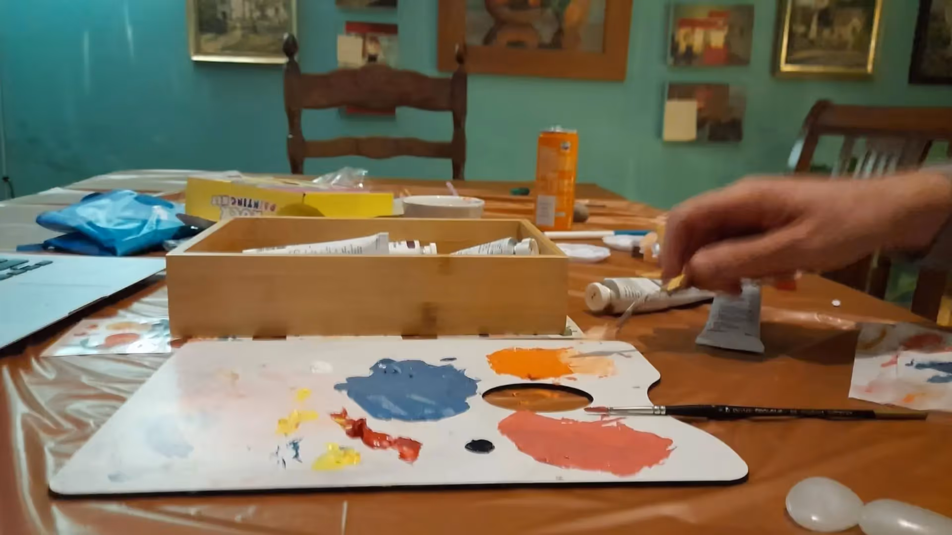 a hand holding a paint brush and a palette on a table