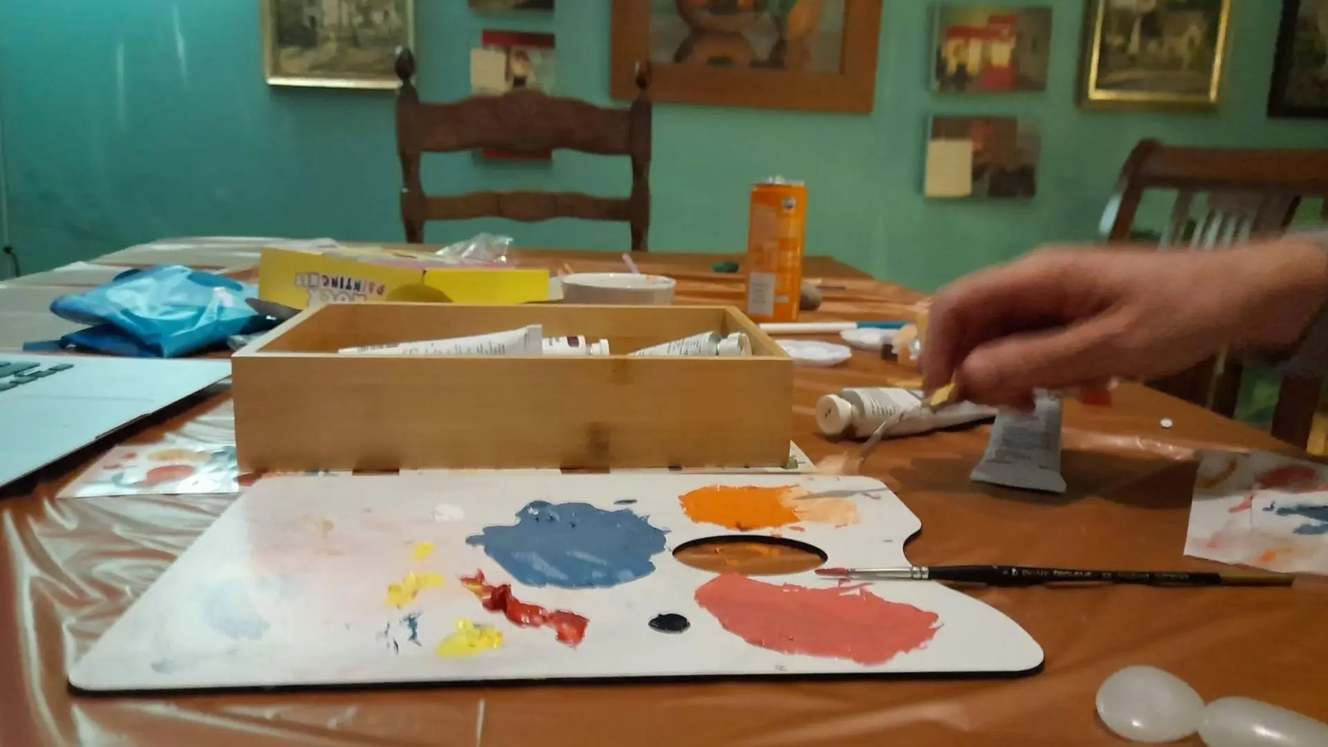a hand holding a paint brush and a palette on a table