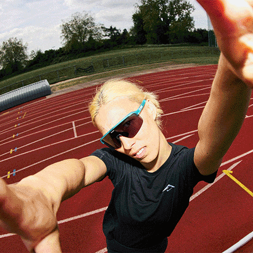 Athlete wearing sunglasses and black sportswear taking a selfie on an outdoor running track.