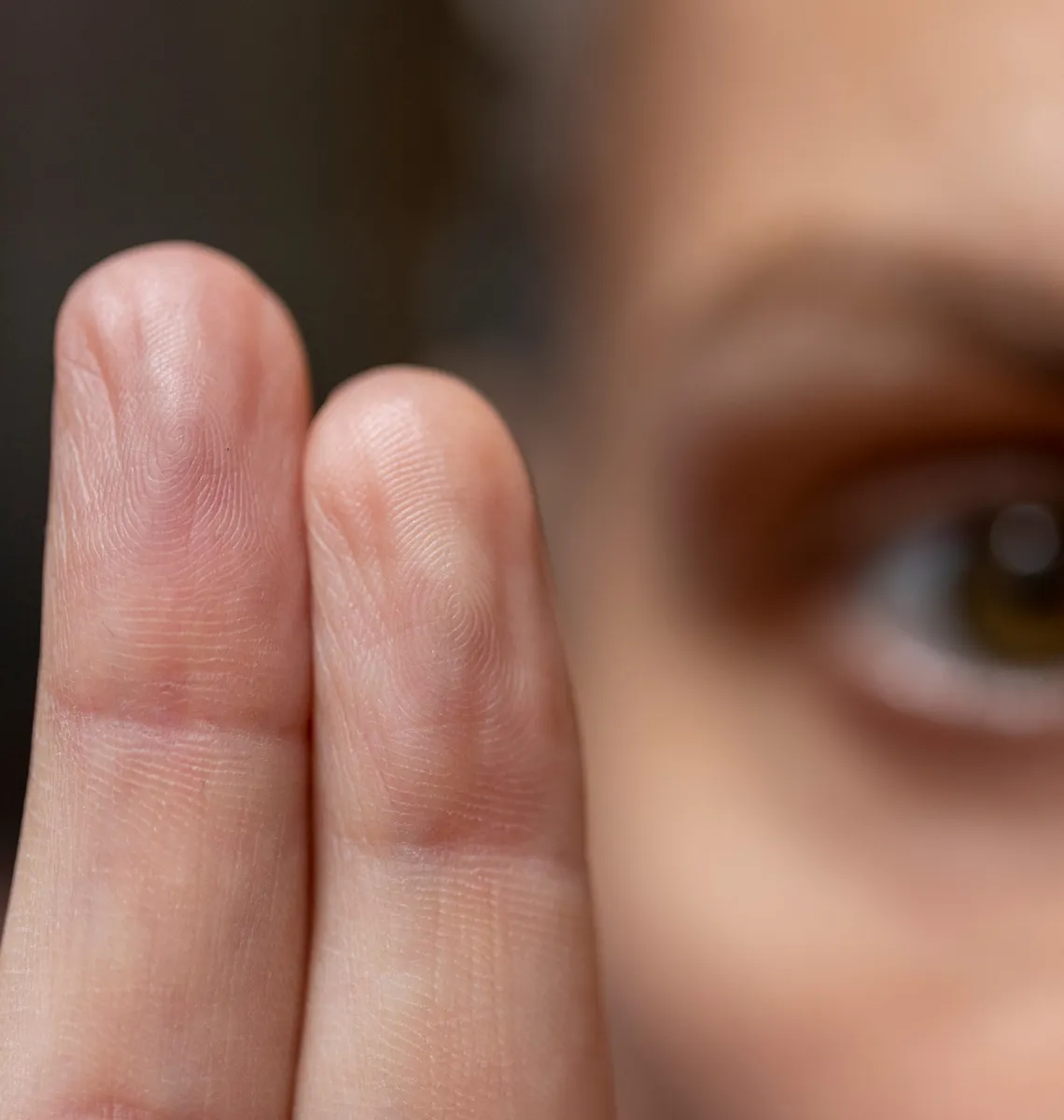 Gros plan de deux doigts levés avec l’œil flou en arrière-plan.