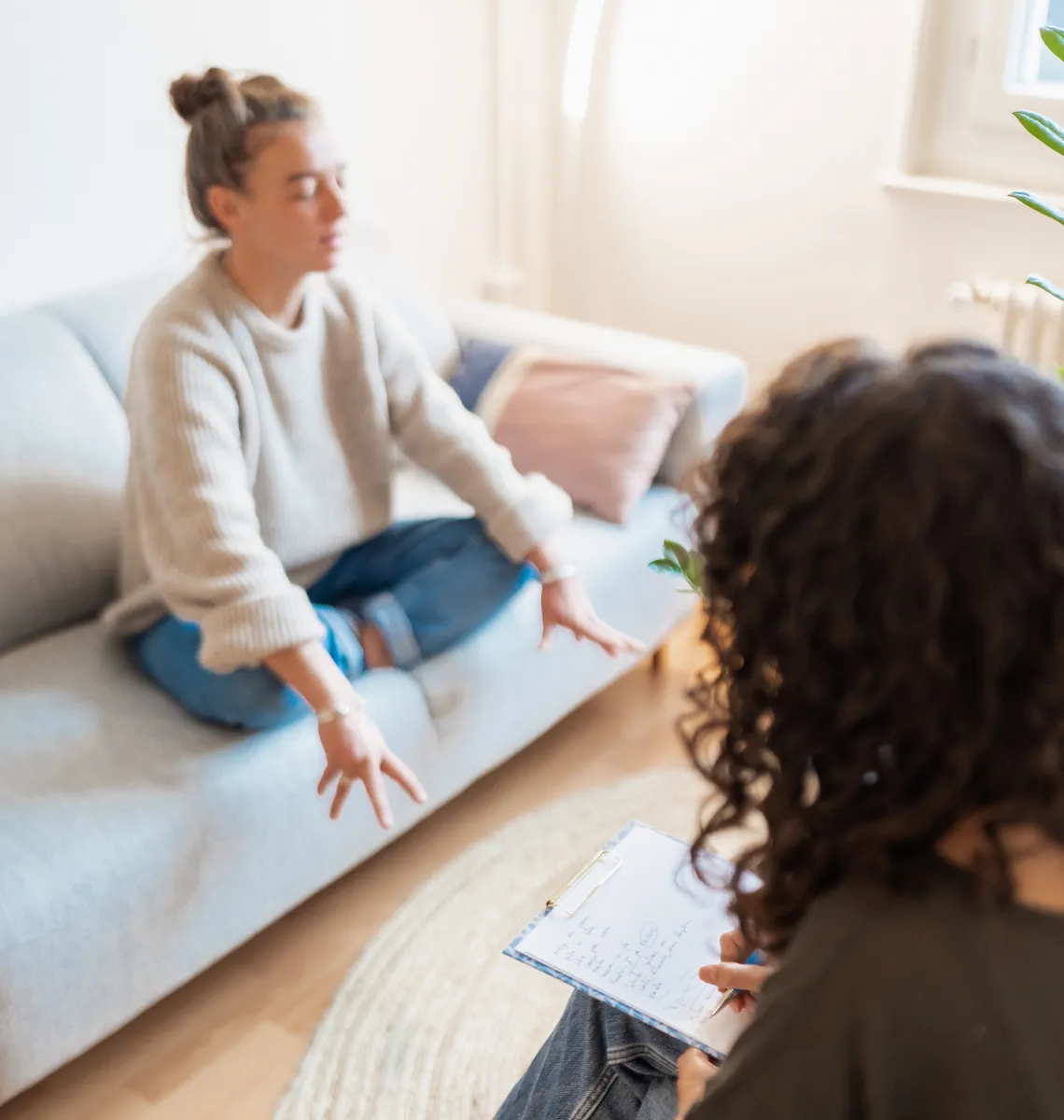 Une femme allongée sur un canapé lors d'une séance de thérapie avec une personne prenant des notes sur un clipboard.