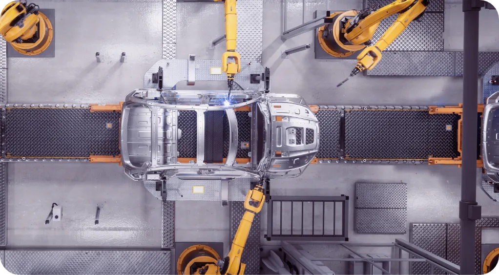 Aerial view of robotic arms assembling a car frame on an automated production line in a factory.