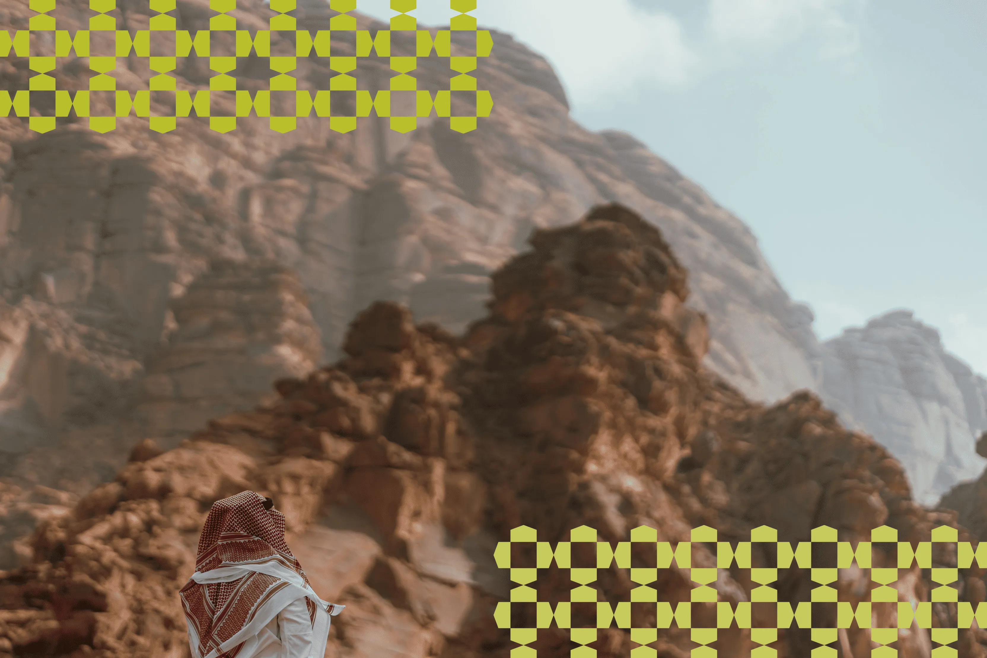Person wearing traditional Middle Eastern clothing standing and looking at rocky desert mountains under a cloudy sky.