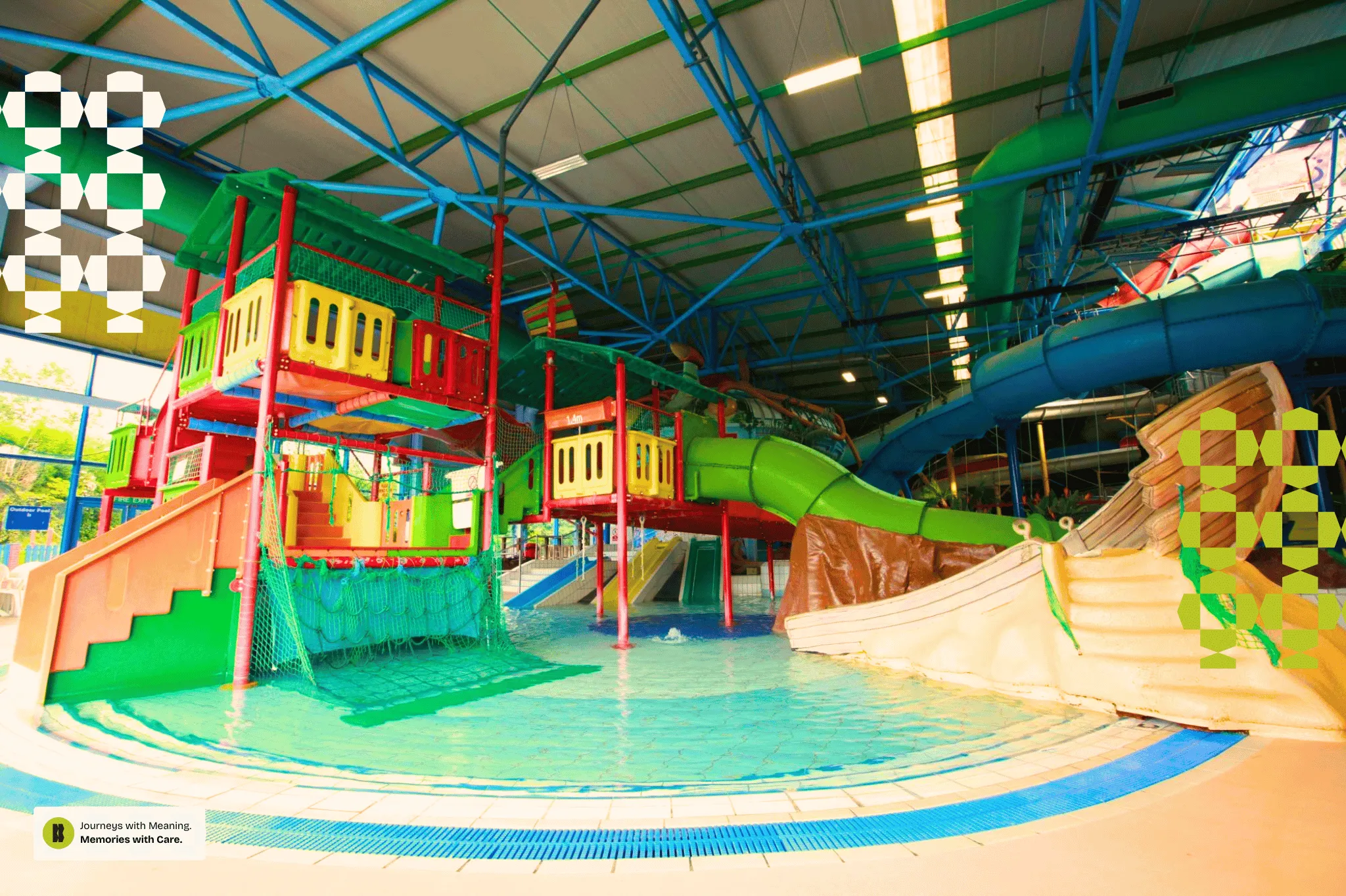 Indoor water park with colorful slides, climbing structures, and shallow pools under a blue steel roof.