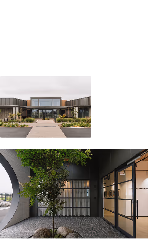 Modern building with large glass windows and landscaped garden in front; lower interior courtyard with small tree and stone flooring beside glass doors.