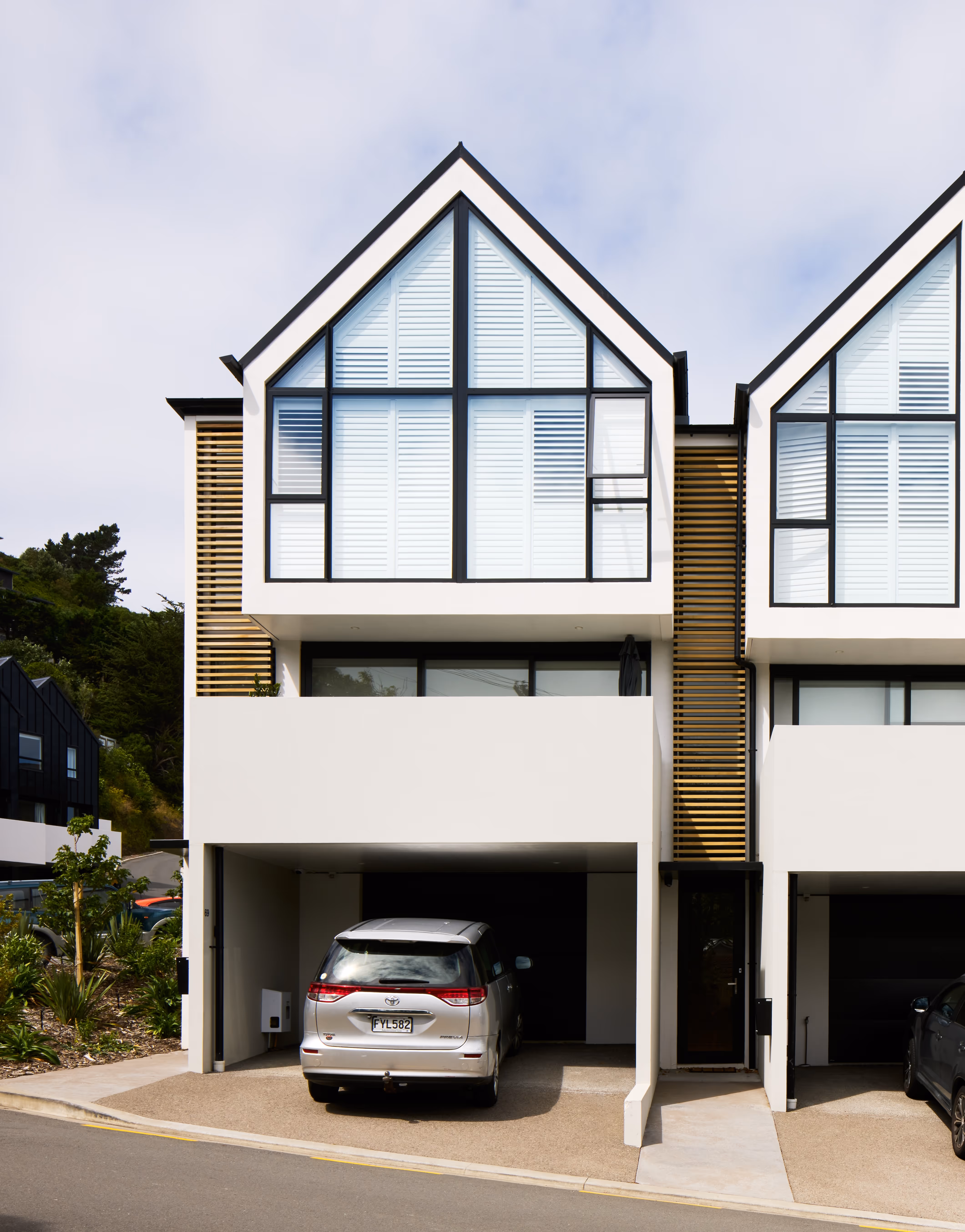 Modern two-story townhouse with large triangular windows, a silver minivan parked in the driveway, and wooden panel accents.